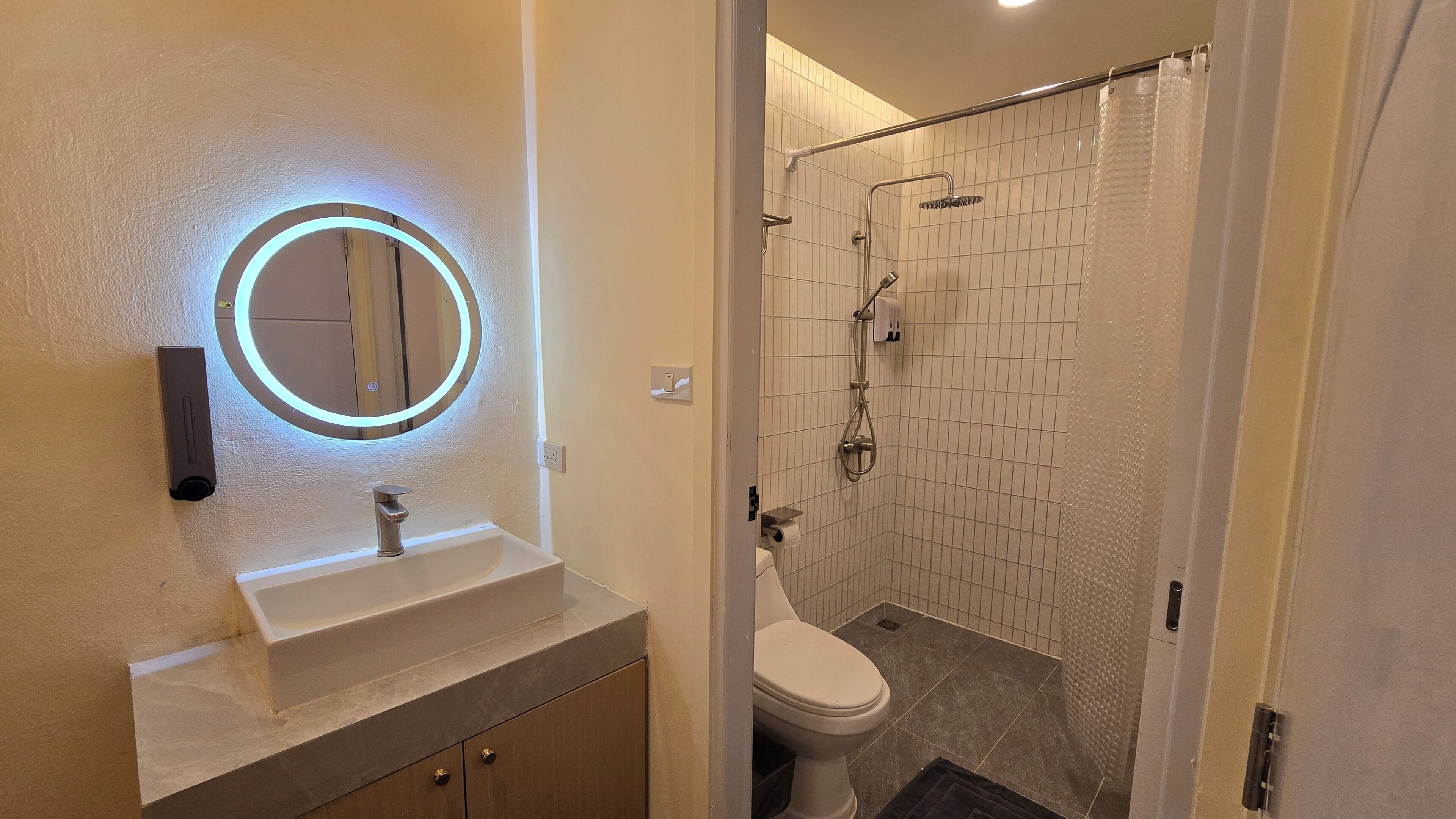 A bathroom with a modern sink, a mirror with a light, a toilet, and a shower area.