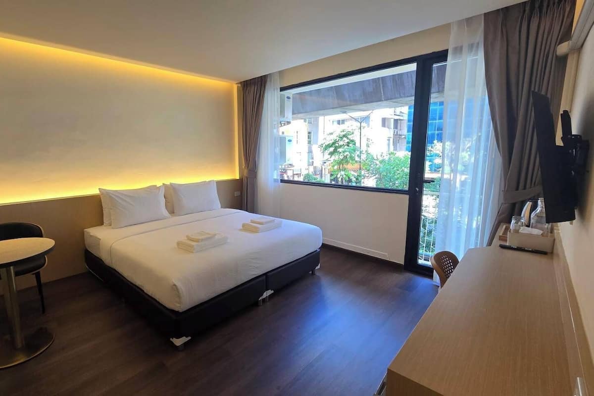 A hotel room with a bed, a small table, a chair, a desk, and a large window with curtains.