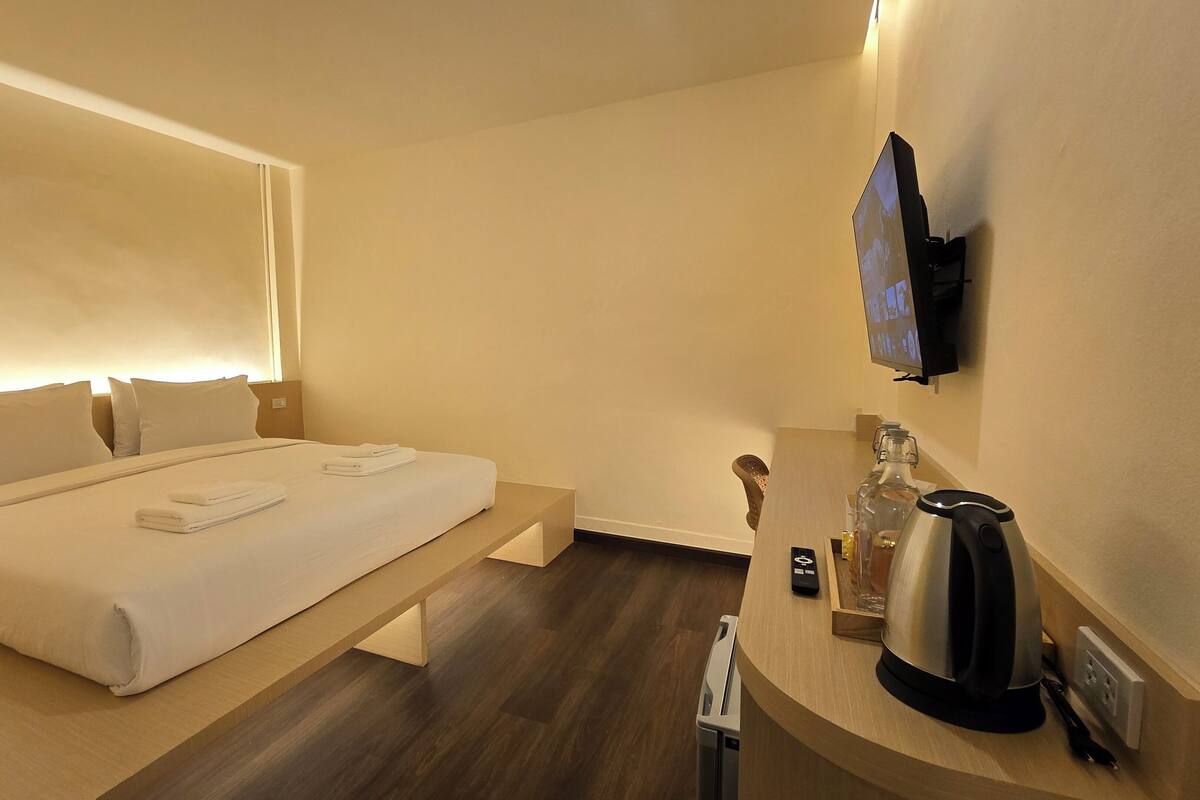 A hotel room with a bed, bedside table, TV, and a coffee maker.