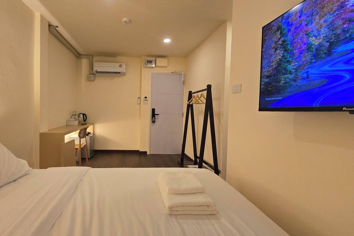 A hotel room with a bed, a desk with a chair, a TV on the wall, and a door.
