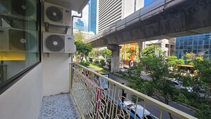 A balcony with air conditioning units, a metal railing, and a view of a busy street with buildings and greenery. - Norns Silom Cafe & Stay (Bangkok)
