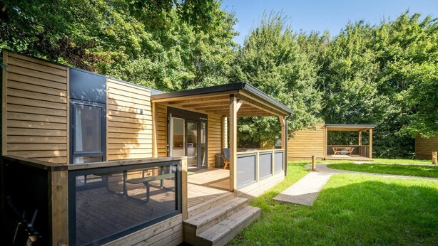 Een houten blokhut met een overdekt terras, een terras en een gazon.
