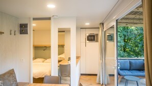 Een moderne kamer met een houten tafel, stoelen, een bed en een balkon met uitzicht op groen.