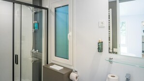 Un baño moderno con cabina de ducha de vidrio, inodoro, lavabo con espejo y perchero para toallas.