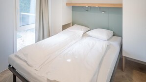Una habitación de hotel moderna con una cama, un ventanal con cortinas, un armario y una lámpara de techo.