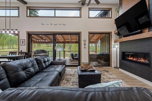 A modern living room with a black leather sofa, a fireplace, and a large TV mounted on the wall.