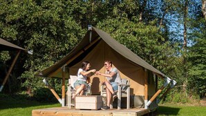 Une petite tente composée d’une seule pièce, dotée d’une terrasse en bois, d’une table et de deux chaises.