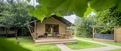 A small, single-story cabin with a deck, a sliding glass door entrance, and a covered outdoor seating area.