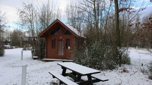 Una cabaña de madera con puerta y ventanas, rodeada de nieve y árboles.