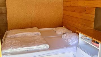 A small, single-bed room with a wooden headboard, a built-in shelf with towels, and a white cabinet.