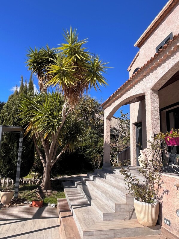 A building with a stone facade, a covered patio area, and a staircase leading to the entrance.