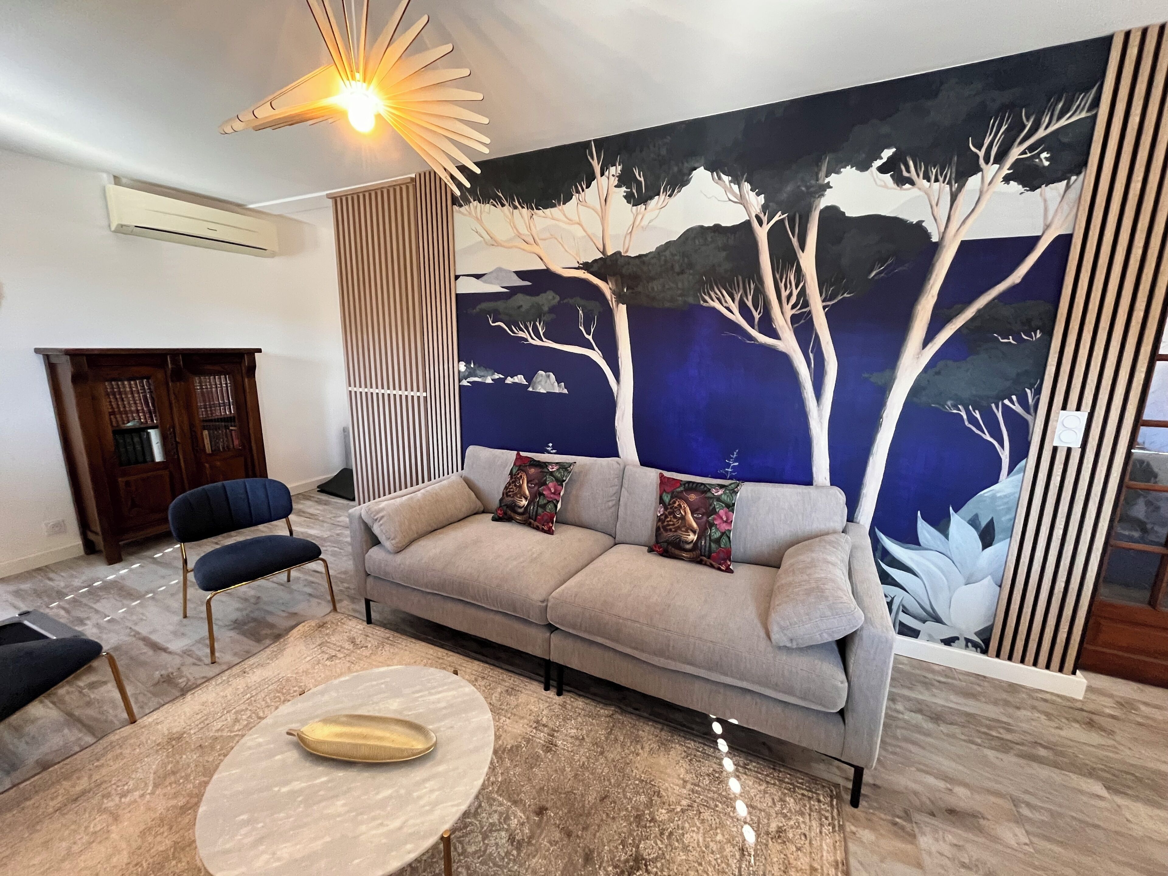 Un salon moderne comprenant un canapé, deux fauteuils, une table basse, une fresque murale et un luminaire au plafond.