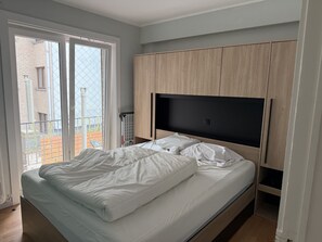 Ein Schlafzimmer mit einem Bett, einem an der Wand montierten Fernseher und einer Glastür zu einem Außenbereich.