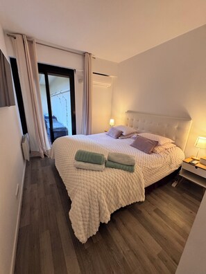 A bedroom with a bed, pillows, a nightstand, a lamp, and a view through a window. - Apartment Cannes Eden luxury residence (Vallauris)