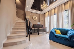 A staircase leading to a second floor, a blue sofa with a yellow pillow, and a chandelier. - Golden Boutique Hotel (T'bilisi)