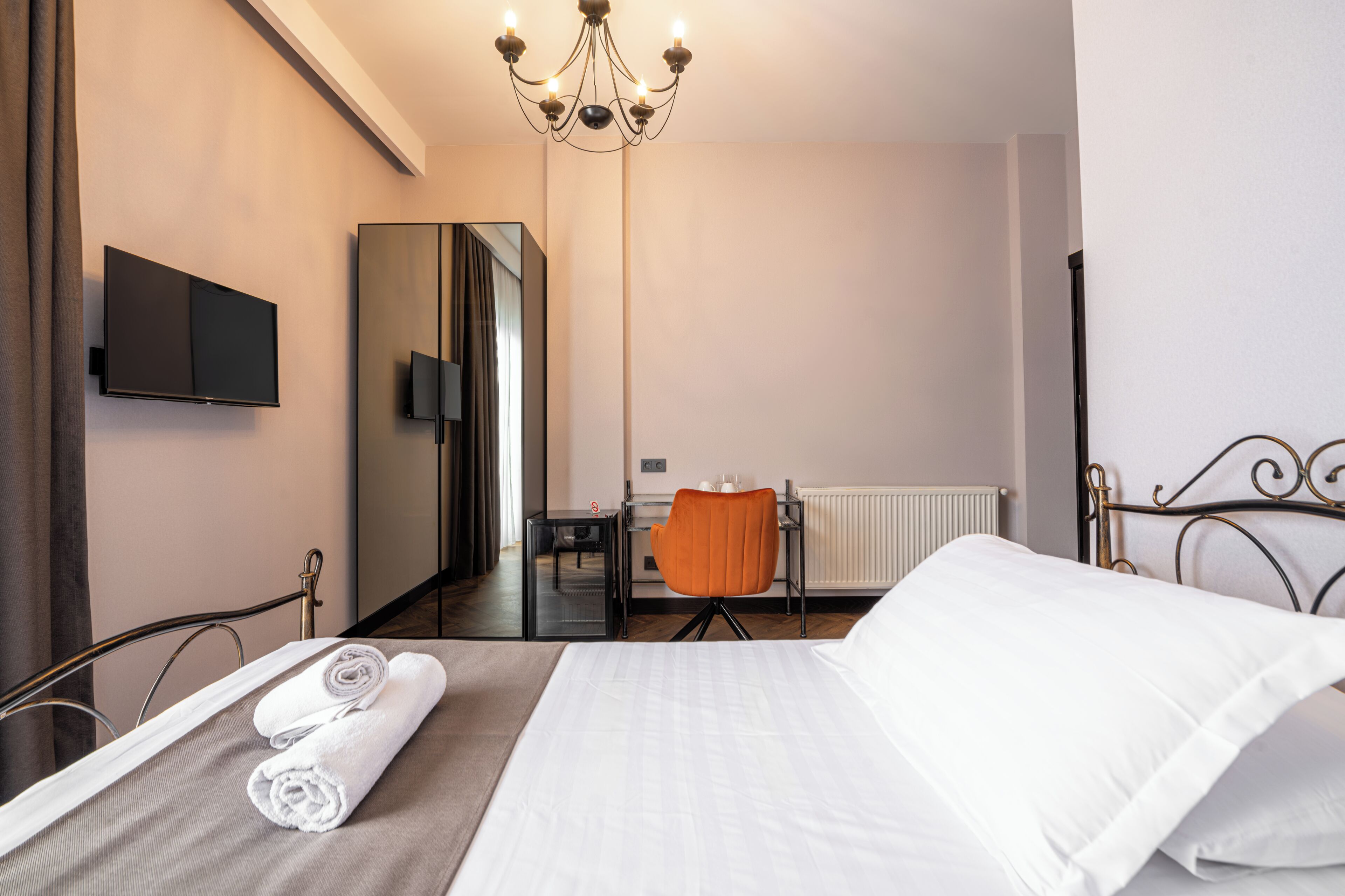 A hotel room with a bed, a chair, a desk, a television, and a radiator.