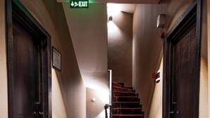 A hallway with a red carpet leading to a staircase, an exit sign, and doors on either side. - Golden Boutique Hotel (Tbilisi)