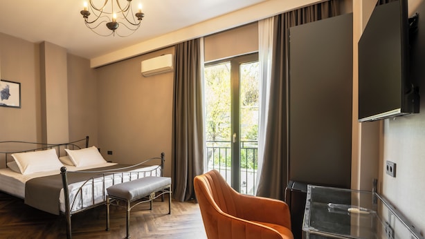 A hotel room with a bed, a desk, a chair, a TV, and a balcony with a view. - Golden Boutique Hotel (Tbilisi)
