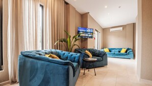 A modern hotel lobby with a large flat-screen TV mounted on the wall, two sofas with yellow cushions, and a potted plant. - Golden Boutique Hotel (Tbilisi)
