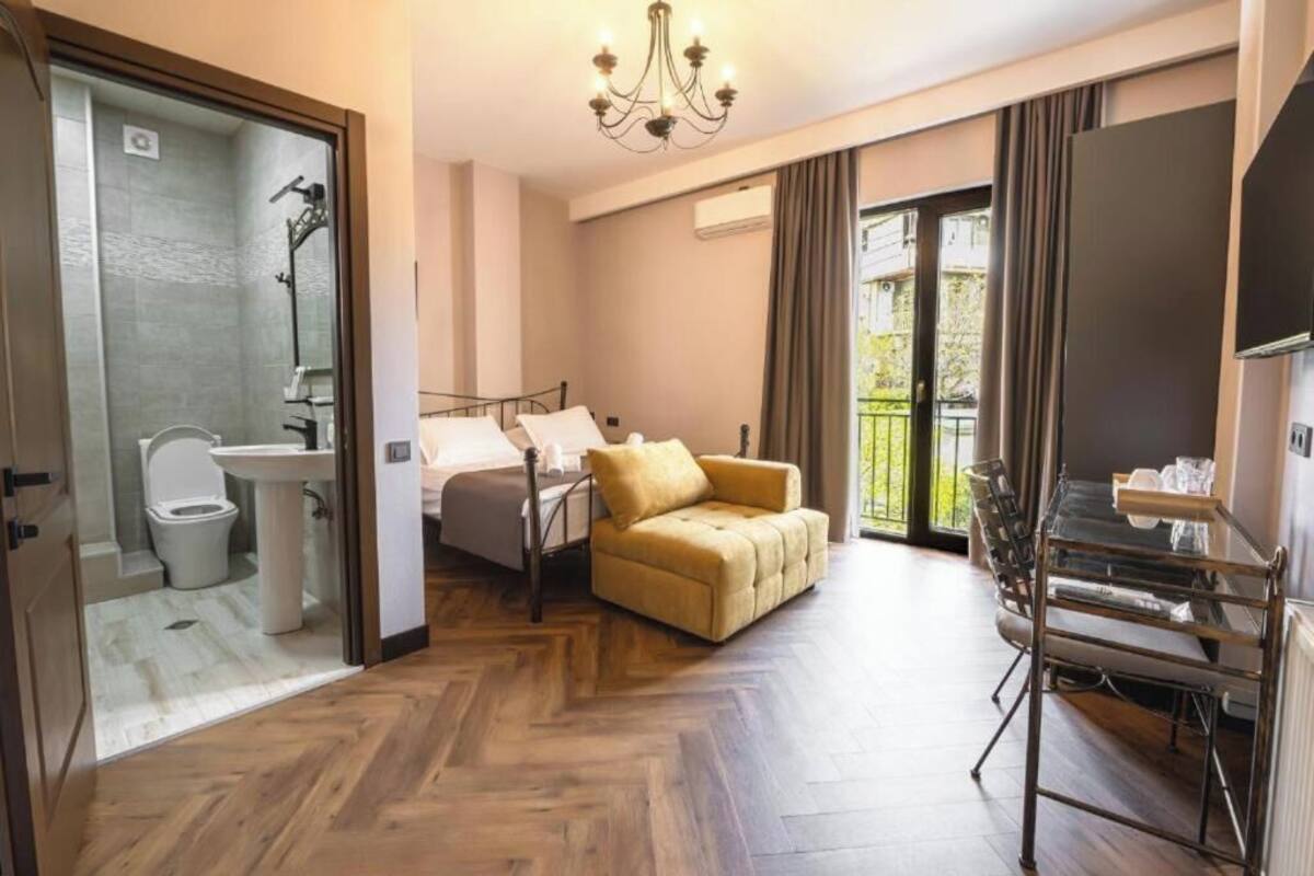 Habitación de hotel con cama, sofá, mesa de vidrio, televisión, ducha y balcón con vistas.