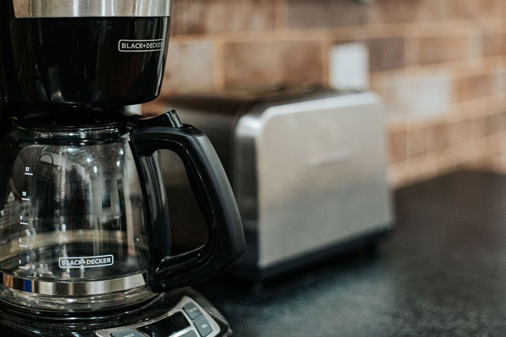 Una cafetera con jarra de vidrio transparente y asa negra, sobre una encimera de cocina.