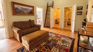 Ein Wohnzimmer mit einer Couch, einem gemusterten Teppich, einem Gemälde und einer Treppe zu einem anderen Raum.
