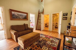Una sala de estar con un sofá, un tapete estampado, un cuadro y una escalera que lleva a otra habitación.