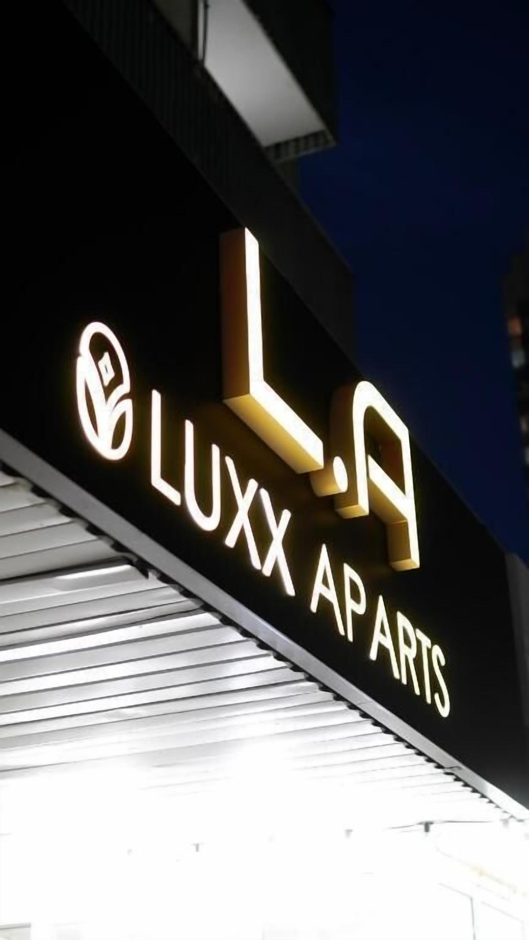 Rakennuksen julkisivussa on valaistut kirjaimet, jotka muodostavat tekstin »LUXX APARTS», ja taustalla näkyy tumma taivas.