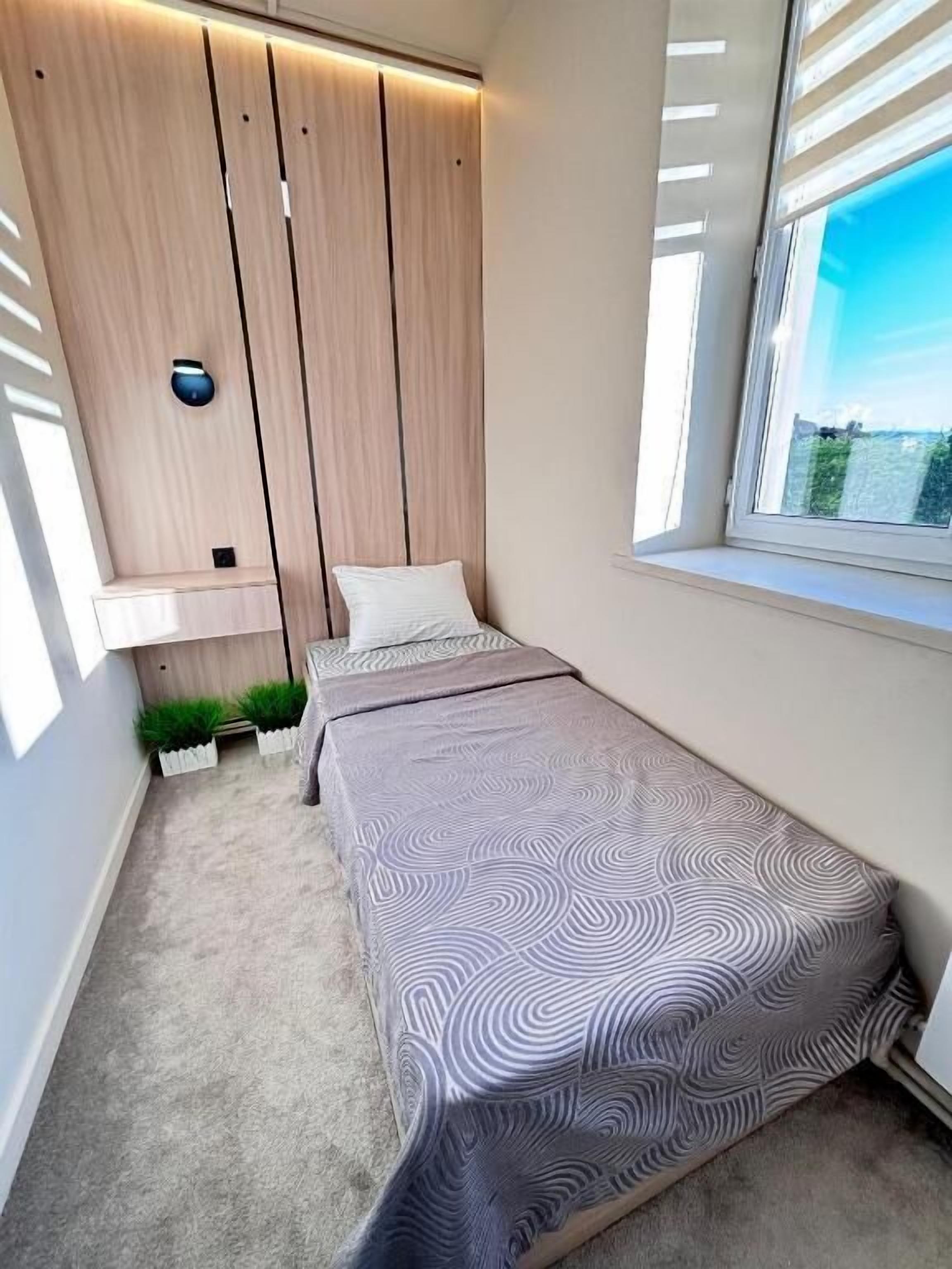Un dormitorio con una cama, una ventana, una lámpara de pared y una planta pequeña.