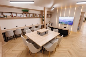 A modern meeting room with a large table, chairs, a TV, and shelves with books and plants.