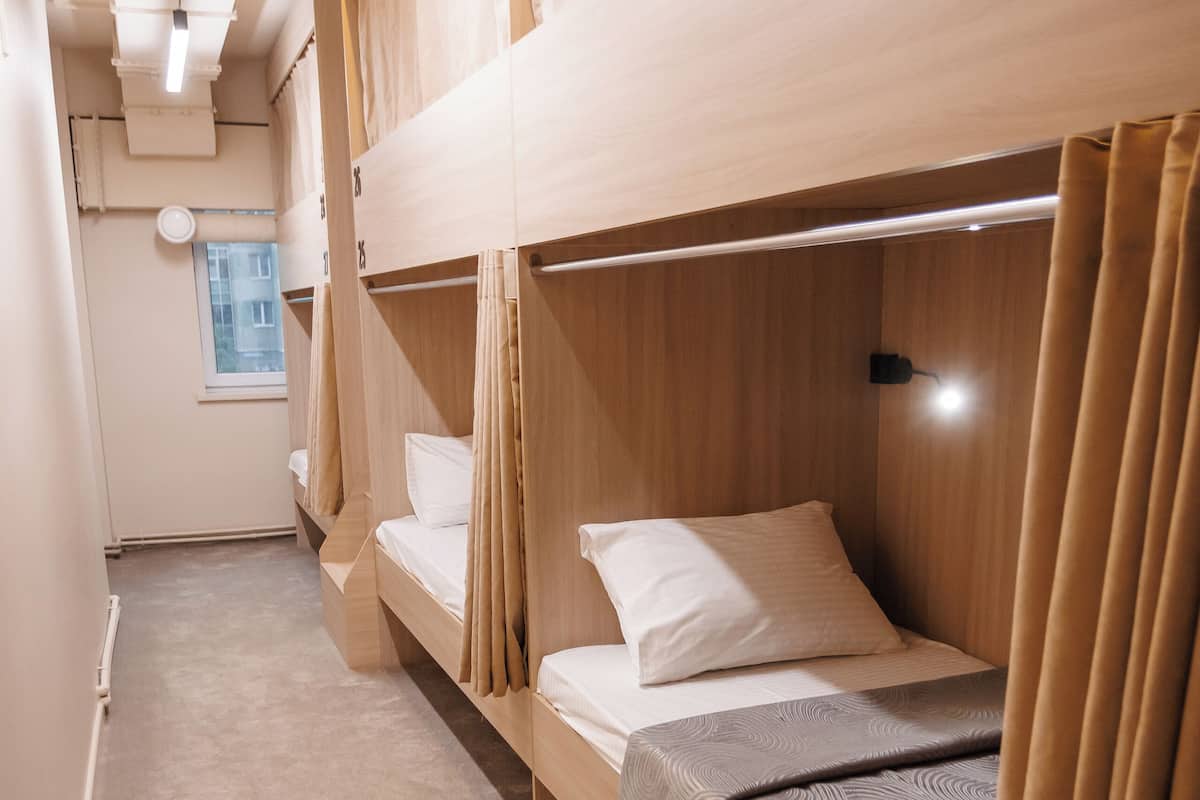 A narrow corridor leading to a room with bunk beds, a window, and a wall-mounted light fixture.