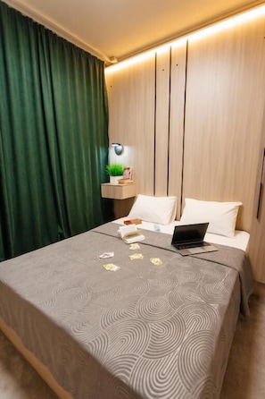 A neatly made bed with a laptop, a bedside table with a plant, and a wall-mounted light fixture.