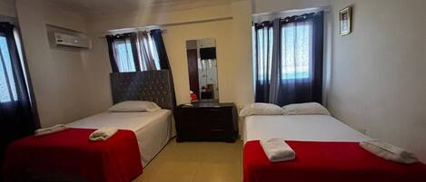 A hotel room with two beds, a dresser, an air conditioning unit, and a mirror.