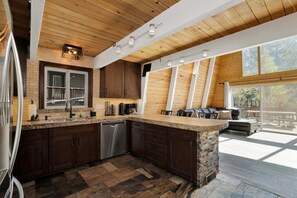 Eine moderne Küche mit einer Steineninsel, Holzbalken an der Decke und einer großen Schiebeglastür, die auf eine Terrasse im Freien führt.