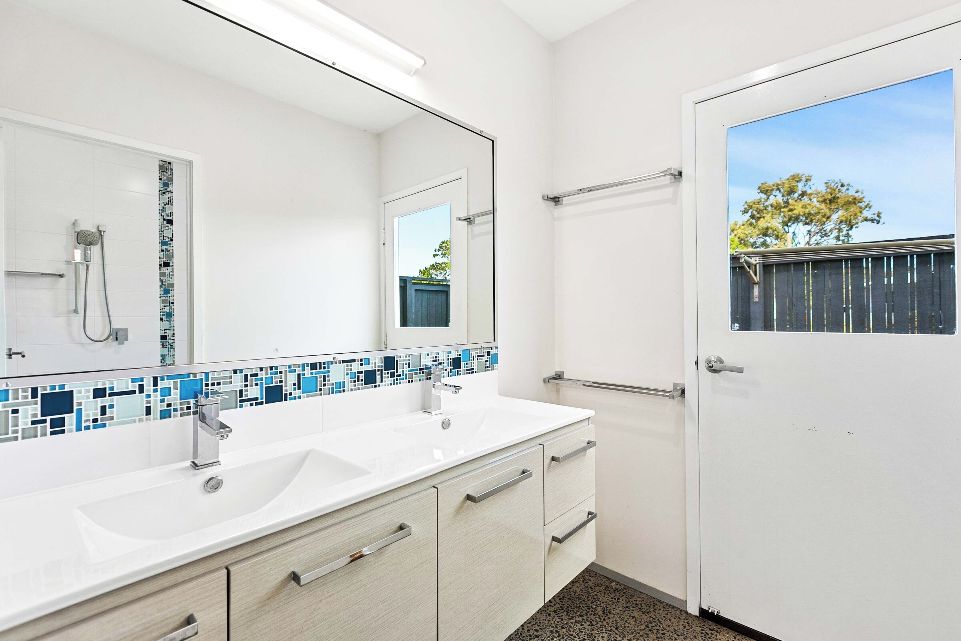 Un baño moderno con un lavamanos blanco, dos cajones, un espejo y una ducha.