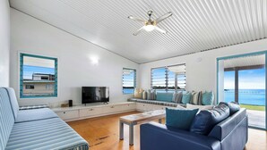 Ein modernes Wohnzimmer mit einer Couch, einem Couchtisch, einem Fernseher und großen Fenstern mit Meerblick.