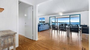 Ein geräumiges Zimmer mit Holzboden, einem Essbereich mit Stühlen und Tisch, einem blauen Sofa und Blick durch große Fenster.