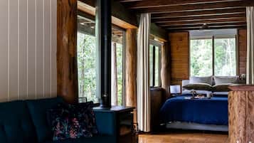 A cozy room with a bed, a sofa, a large window, and a wooden ceiling.