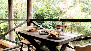 An outdoor wooden table set with food and drinks, surrounded by a wooden fence and lush greenery.