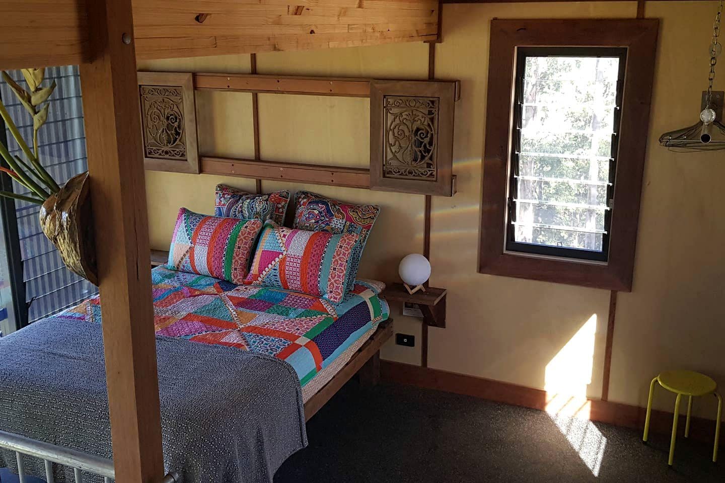 Une chambre confortable avec un lit, des coussins aux couleurs vives, une table de chevet avec une lampe et une fenêtre donnant sur un beau paysage.