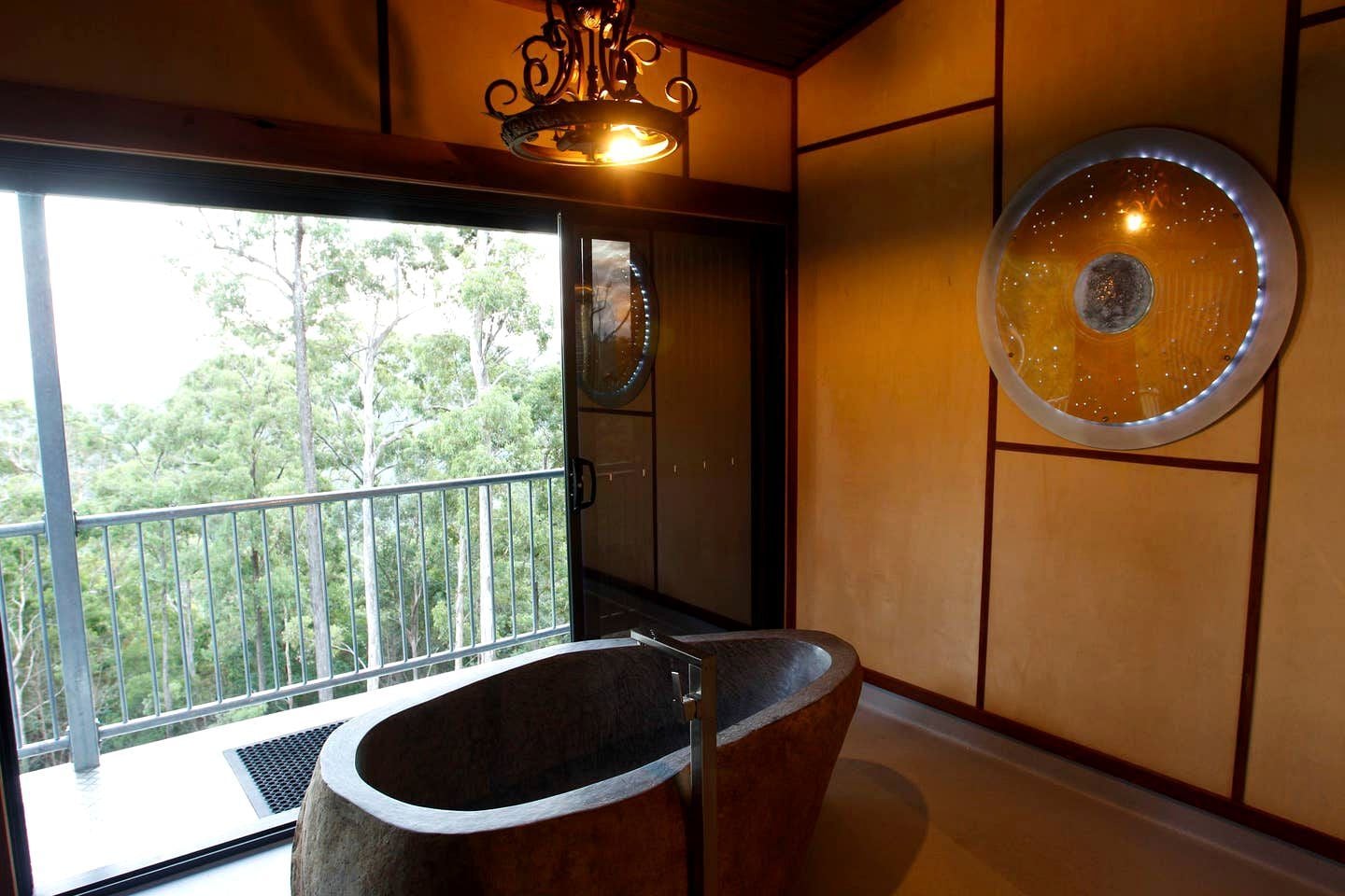 A bathroom with a large bathtub, a balcony with a railing, and a view of trees outside.