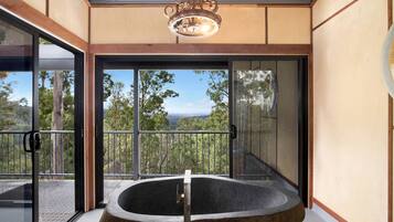 A modern bathroom with a freestanding bathtub, large glass doors, and a view of the surrounding landscape.