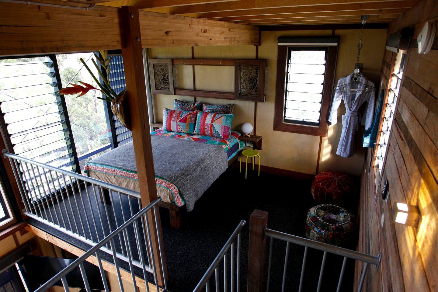 A bedroom with a bed, a window, a hanging rack, and a small stool.