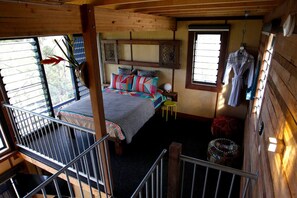 Ein Schlafzimmer mit einem Bett, einem Fenster, einem Kleiderhaken und einem kleinen Hocker.