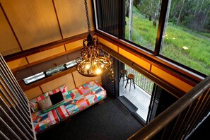Una habitación con un banco acolchado de colores, una lámpara colgante y vistas a un área verde exterior a través de amplios ventanales.