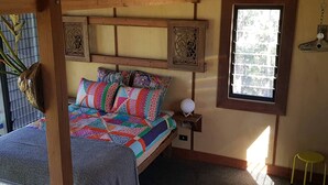 A cozy bedroom with a bed, colorful pillows, a bedside table with a lamp, and a window with a view. - Gorgeous Queensland Tree House with Great Views Perfect for Glamping, Gold Coast (Gold Coast)
