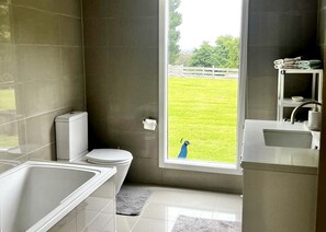 Un baño con inodoro, bañera y lavamanos, con vista a un césped verde y una valla.