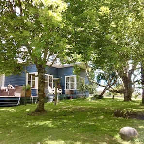 A house with a blue exterior, a covered porch, and a lawn with trees. - Whispering Waters: Family-Friendly Cottage Rental in Tanybryn with Nearby Waterfalls (Tanybryn)
