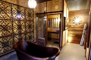 Une salle de bain avec une baignoire sur pieds, une douche avec une porte en verre et un mur en bois agrémenté d’un luminaire décoratif.