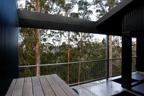 A balcony with a metal railing, a wooden table, and a view of trees. - Stunning Tree House with Pool Access Ideal for Luxury Holiday Accommodation, Gold Coast (Gold Coast)